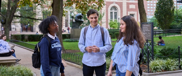 Three students, one of whom wears a Columbia Law sweatshirt, chat in front of the Thinker statue.