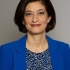 Pictured above is Caline Mouawad. She has dark brown bob. Silver studs and a silver neckless hang off her ears and neck. She is wearing a royal blue blazer and a patterned blouse. She has brown eyes. 
