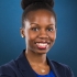 Pictured above is Temitope K. Yusuf. She is wearing a royal blue shirt under a navy blue blazer. She has pearl studs in each ear. She is smiling wide, and has wine colored rouge on her lips. She has dark brown eyes and curly hair tied back into a bun. 