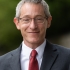 Professor Josh Gupta-Kagan, wearing glasses, a grey jacket, and a red necktie, smiles.