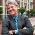 Image of Katherine Franke, looking away while smiling, with arms crossed, wearing a grey suit and blue shirt