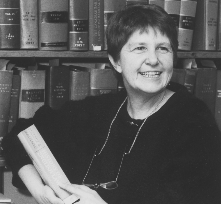 black and white photo of a woman in front of bookcases holding a book 