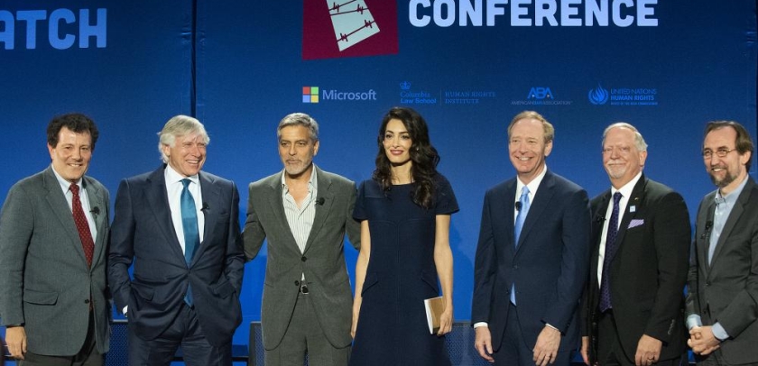 6 men in suits flank a woman in black dress