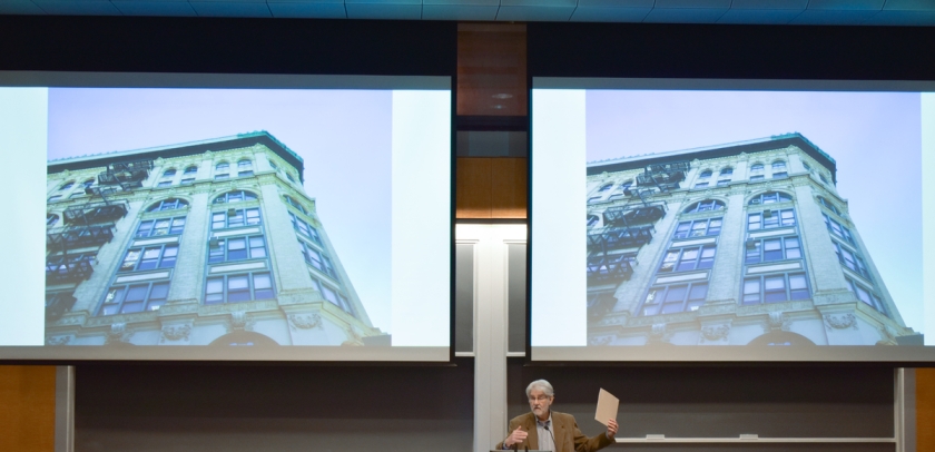 Professor Vincent Blasi gestures in front of a screen featuring a multistory building.
