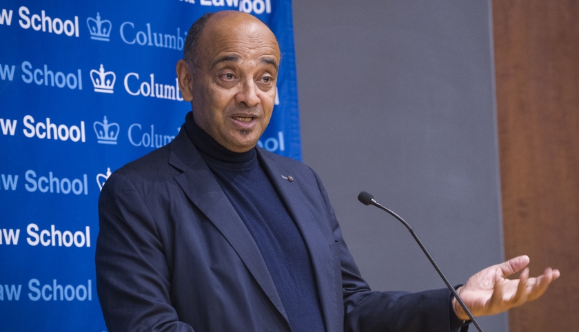 Man speaking at microphone gestures.