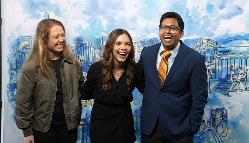 Two women and a man in front of a painted mural
