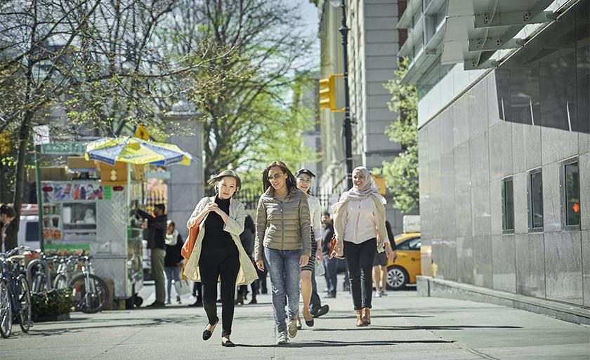 Students walk in front of Jerome Greene Hall next to a halal cart and taxi.