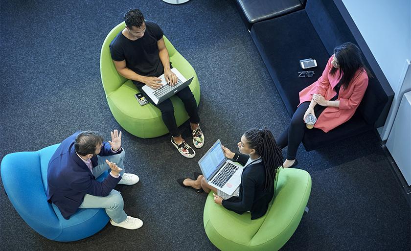 Students sit a circle of brightly colored chairs.