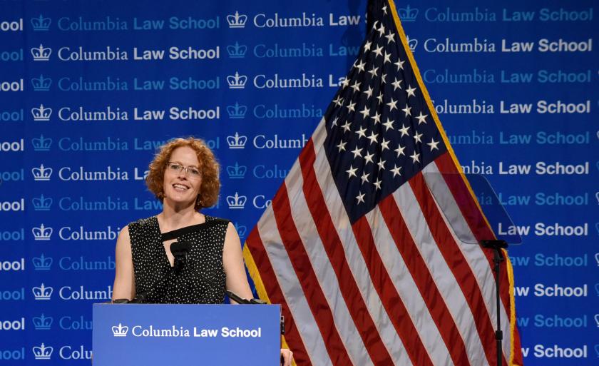 Dean Gillian Lester speaks at a podium in front of a backdrop that says Columbia Law School, next to an American flag.