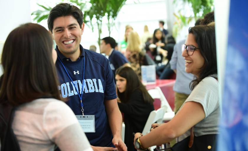 A student wearing a Columbia sweatshirt smiles at another student.