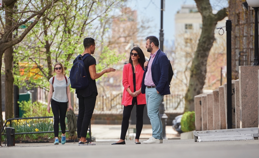 Three students talk on a sidewalk