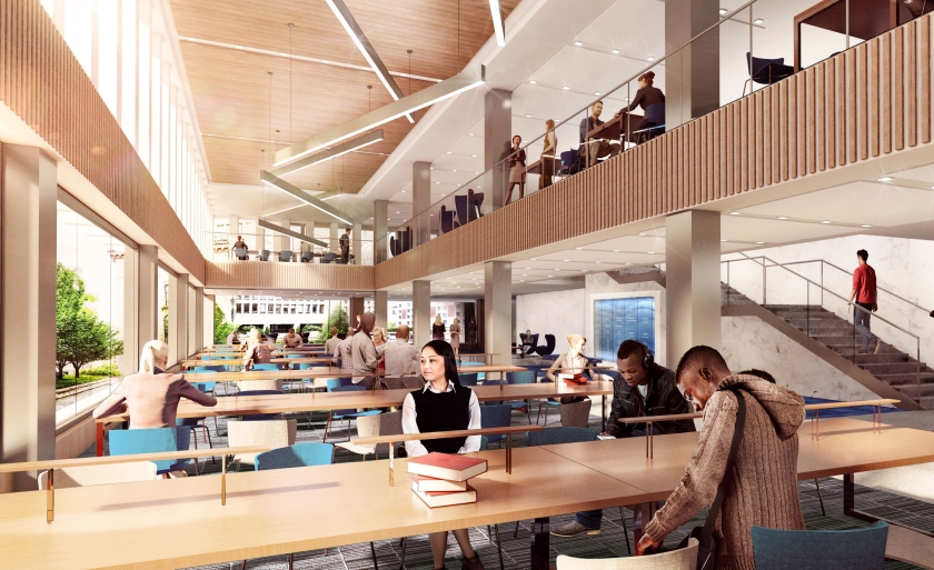 Students sit at long tables next to a bank of windows and beneath a mezzanine.