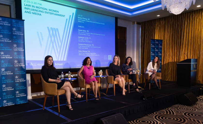 A panel of five speakers sits in chairs on a stage.
