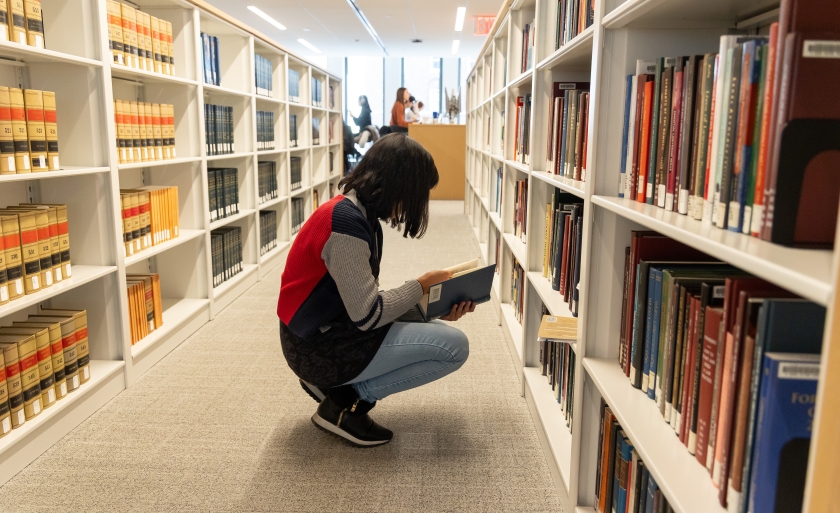 Student reading a book next to bookshelves