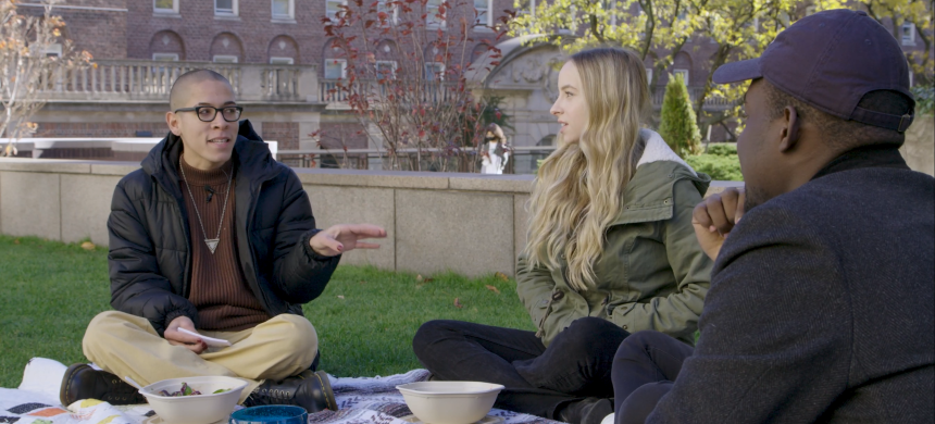 Three students sitting on a lawn talking