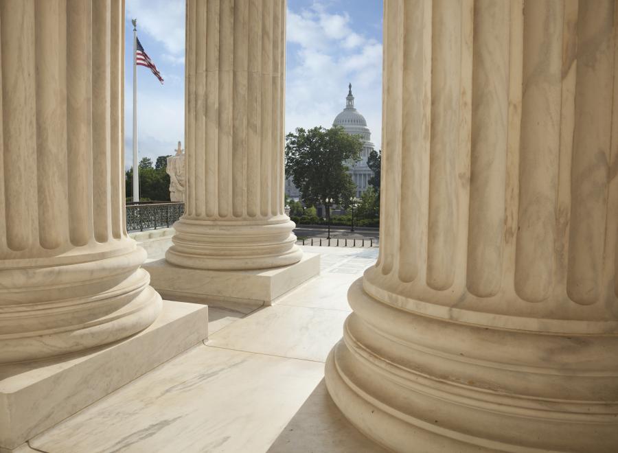 Close up of the columns of the Supreme Court building with an American flag and the US Capitol in the background