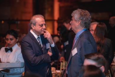 Two men in suits talking at crowded event