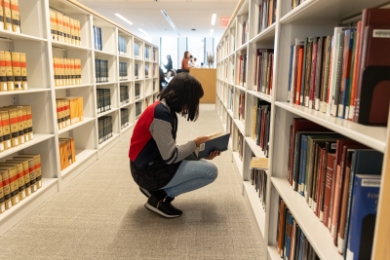Student reading a book next to bookshelves