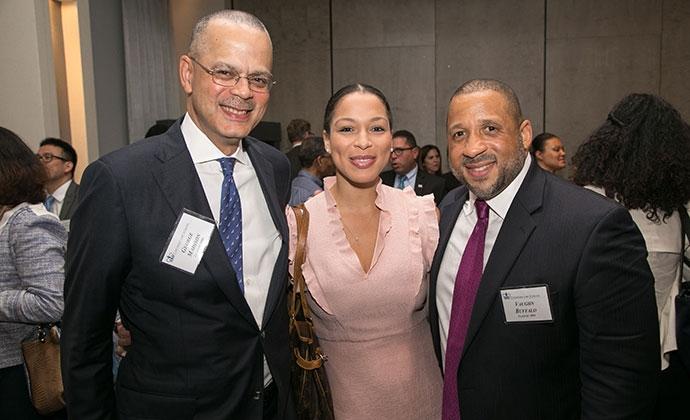 A woman in a pink dress is flanked by two men in suits