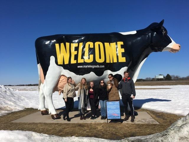 Student pose next to a cow sculpture in a snowy field.