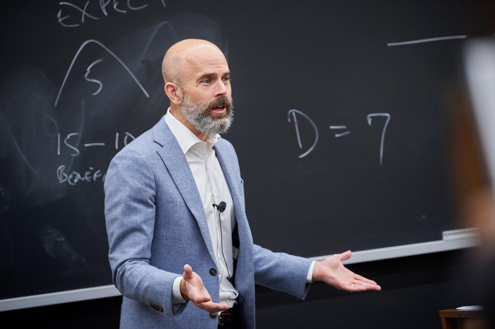 Professor Ed Morrison gestures in front of a blackboard.
