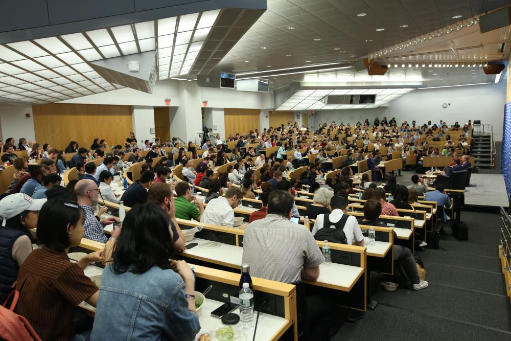 A packed lecture hall with Brad Smith, Tim Wu, and Dean Lester on stage.