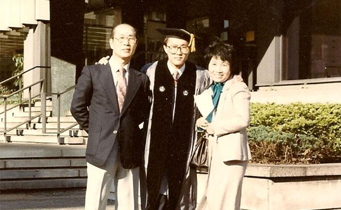 Don Liu stands between his mother and father while wearing a cap and gown.