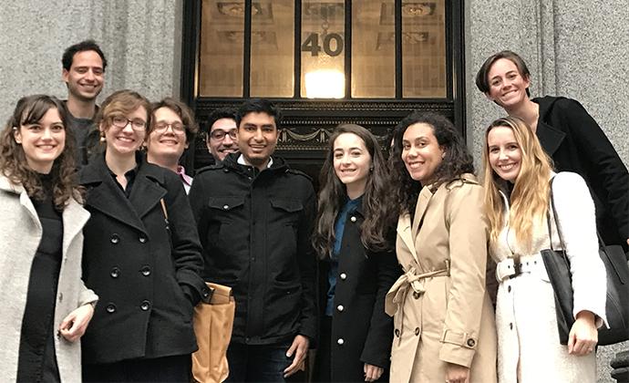 A group of ten students in business attire pose outside a courthouse, smiling.