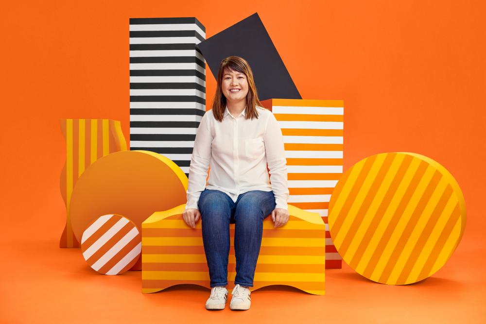 Jennifer Fitzgerald sits on some orange geometric shapes.