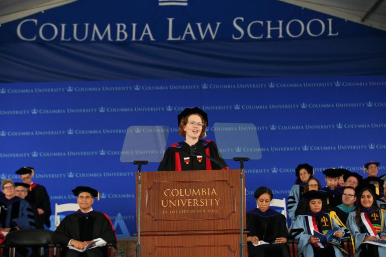 Dean Lester stands behind the podium wearing academic regalia.