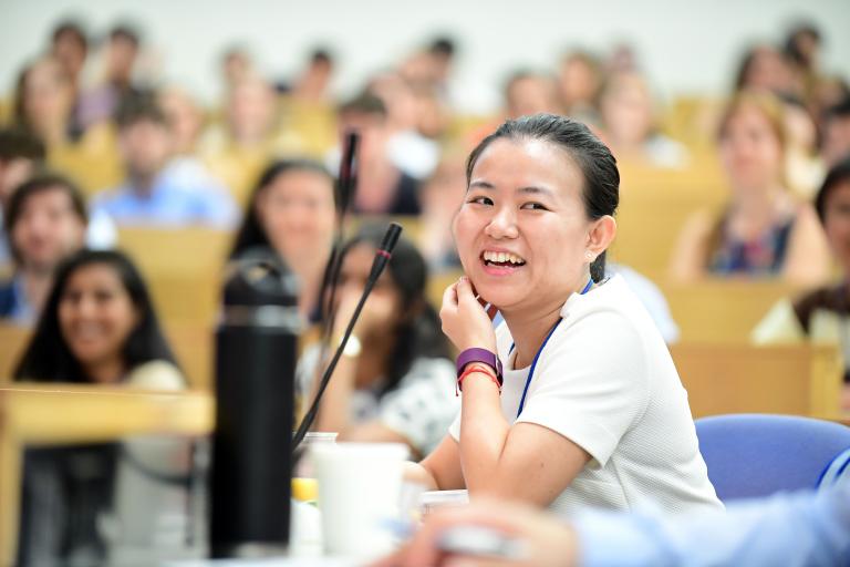 A student smiles at a microphone in a lecture hall.
