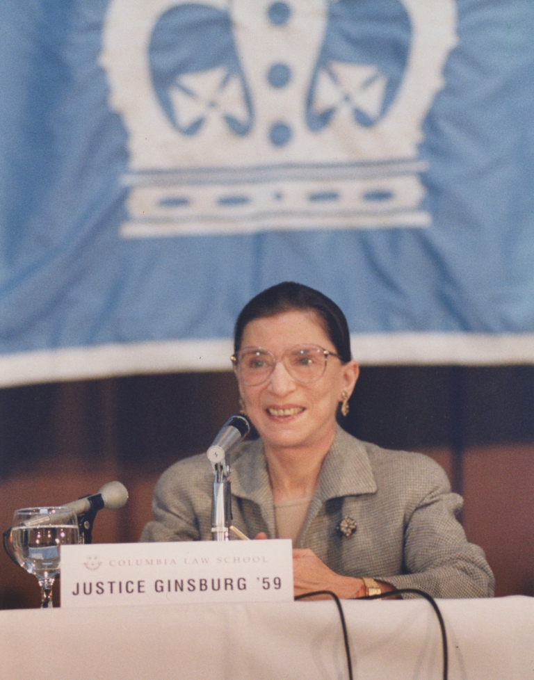 Ruth Bader Ginsburg ’59 sitting in front of a Columbia Law banner
