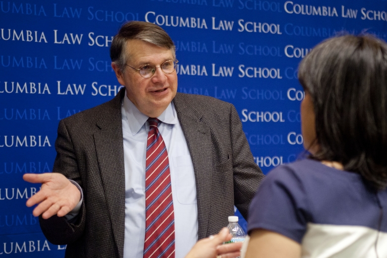 Professor Thomas Merrill in jacket and tie talking to student