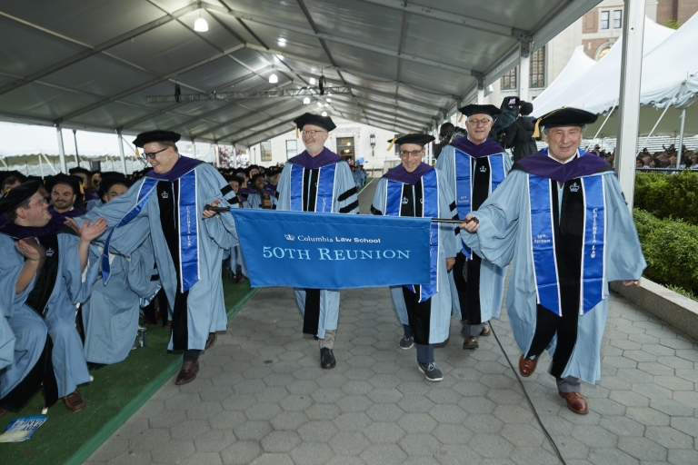 Five older men in caps and gowns carrying 50th Reunion sign