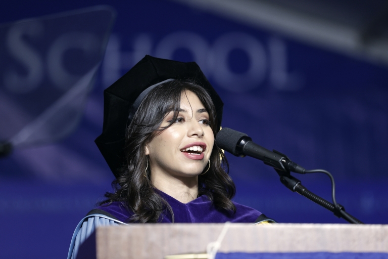 Woman in cap and gown before microphone at podium