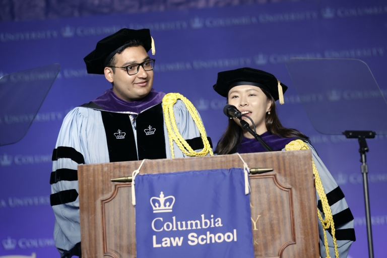 Man and woman in caps and gowns behind Columbia Law School podium