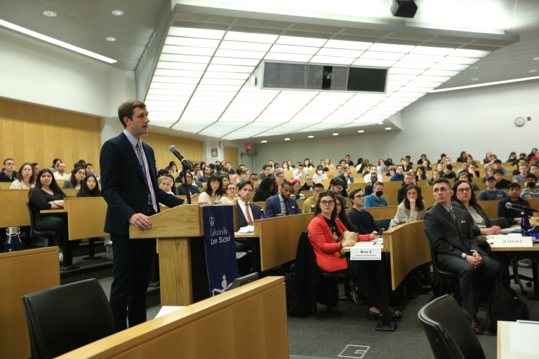 Man standing at a podium in a classroom with audience members seated