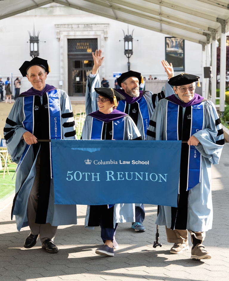 Four people in academic gowns carrying a Columbia Law banner