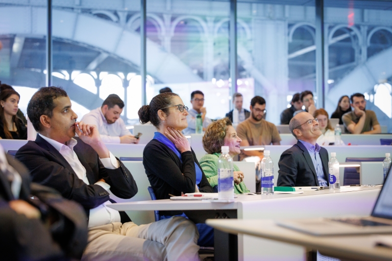 Two women and two men watching a presentation, seated in a classroom