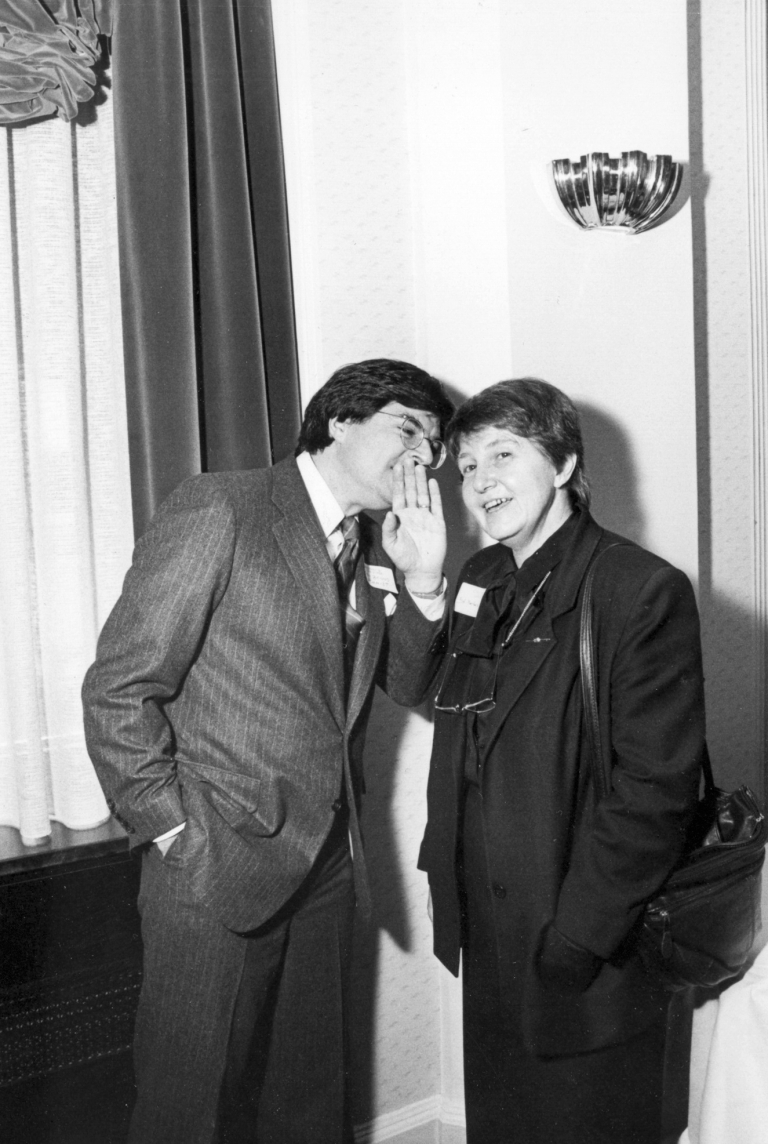 A black and white photo showing a man whispering to a woman