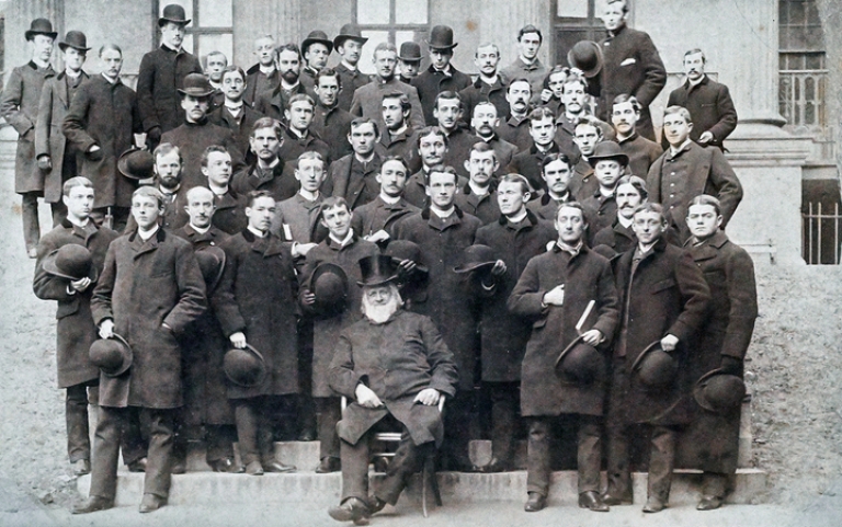 Theodore White with white beard and top hat surrounded by students in overcoats
