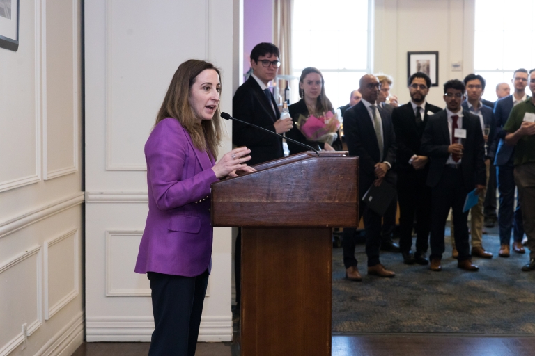 A woman in a purple jacket speaking at a podium