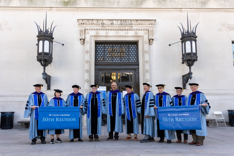 Ten members of the Classes of 1971 and 1976 in academic regalia holding 50th and 55th reunion banners as they stand in front of Butler Library
