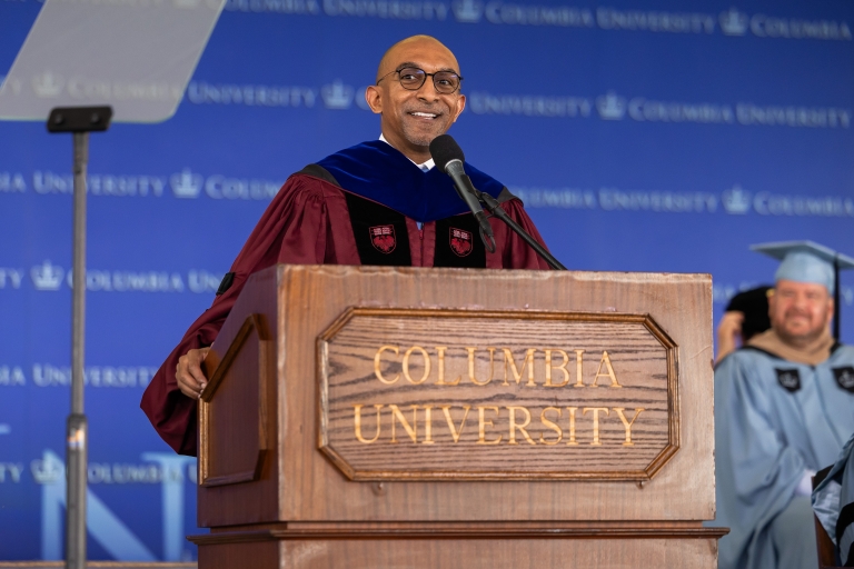 Dean Daniel Abebe in crimson academic robe behind a Columbia University podium