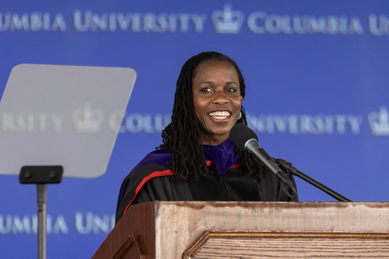 Professor Olatunde Johnson in black robe at a podium in front of a microphone