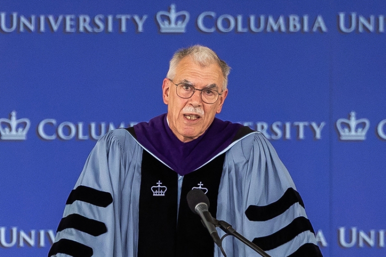 Donald B. Verrilli Jr. in Columbia blue graduation regalia behind a microphone