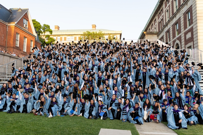 The entire class of2026 in their blue graduation gowns on bleachers tossing their tams in the air
