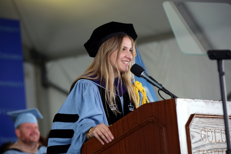 Beatrice Olivieri in academic regalia before a microphone