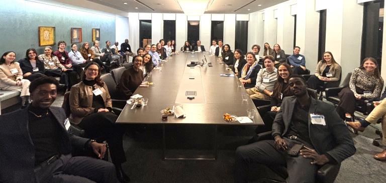 Photo of current and past Berger Fellows at 2026 networking event. About forty people are shown in a boardroom, sitting around a long table and in chairs lining the walls. They are looking at the camera and smiling.