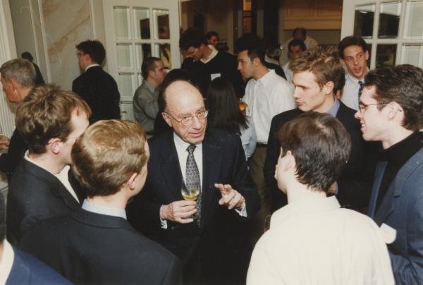 Man in suit and tie talks to a group of people at an event